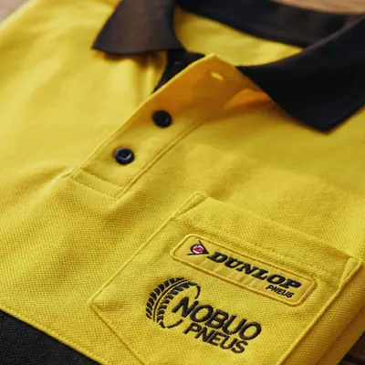 Polo amarela e preta com os logos da Dunlop e da Nobuo Pneus bordados no bolso