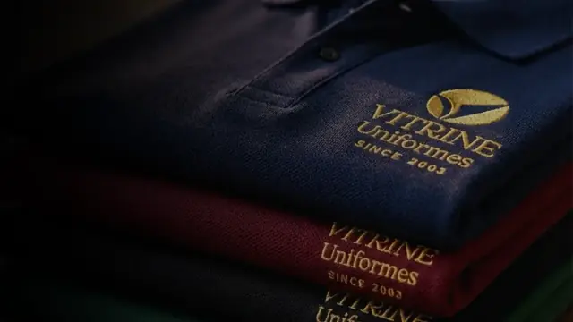 Camisas polo empilhadas com o logo da Vitrine Uniformes bordado em dourado
